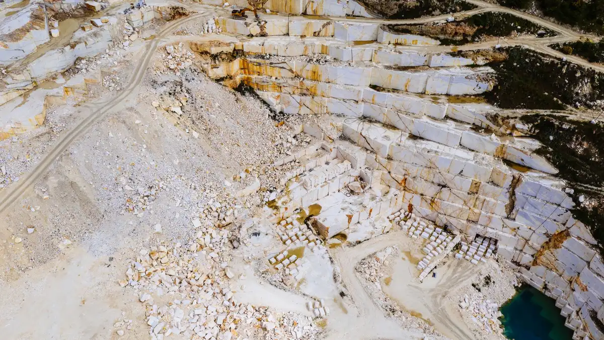 Cava di pietra con macchinari di estrazione in paesaggio naturale, mostrando l'impatto ambientale dell'estrazione